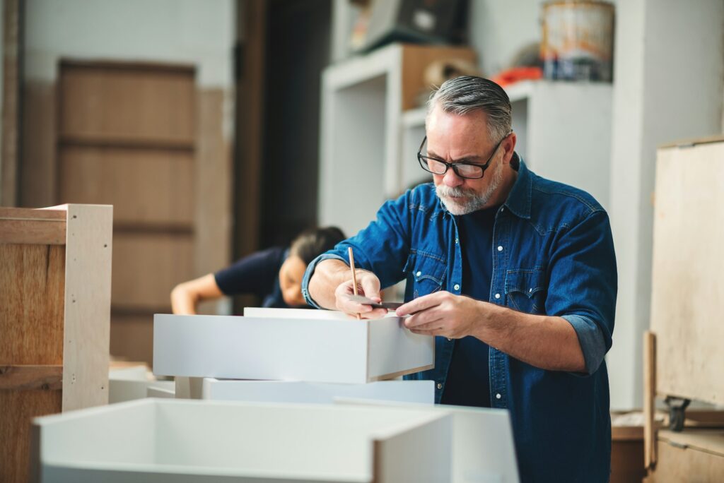 Senior caucasian man specialist worker measuring white shelf furniture in wood workshop